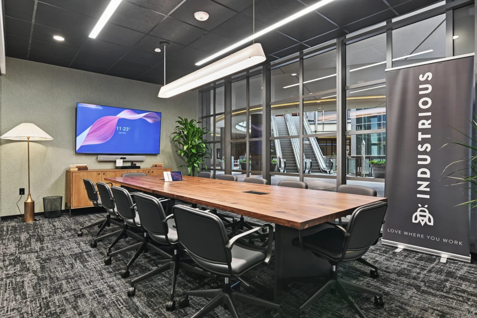 Conference room at Industrious Sherman Oaks with a long walnut table, black chairs, a wall screen, plants, and floor-to-ceiling glass